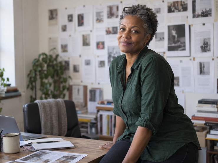 Nadia Osei photographed at her desk in front of a wall of pinned page proofs