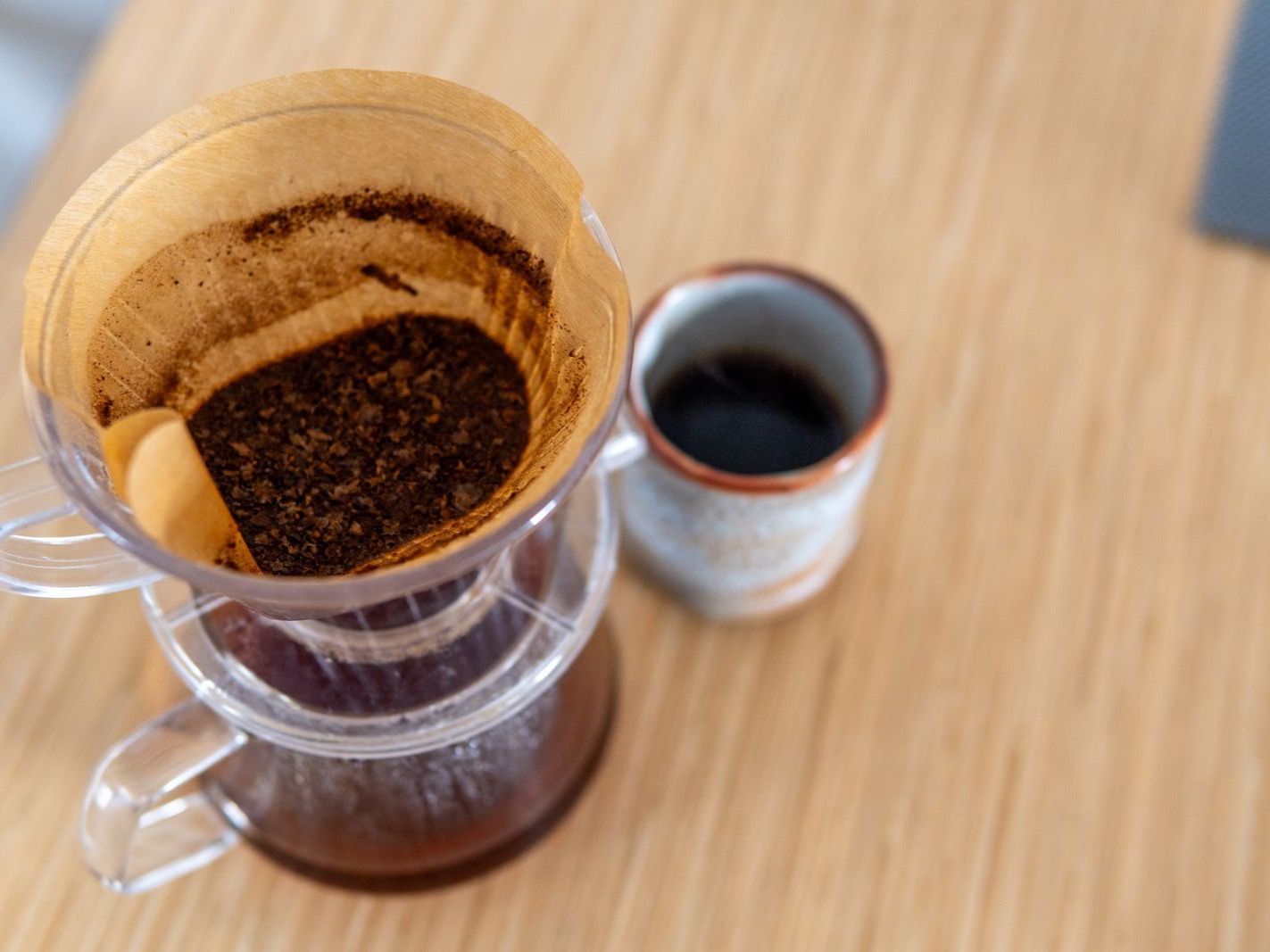A pour-over cone of ground coffee beside a cup of black filter coffee