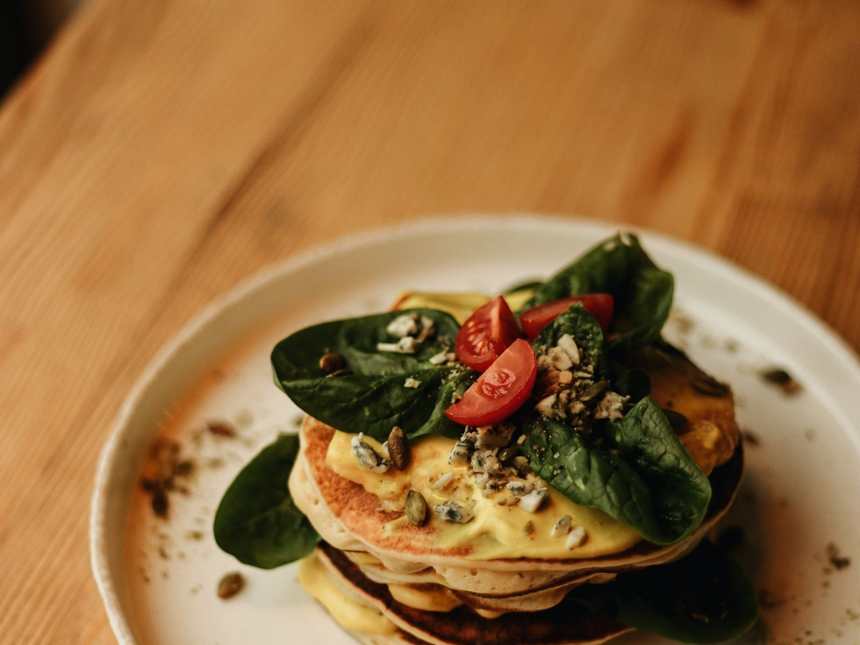 A stack of pancakes dressed with tomatoes and seeds on a wooden table