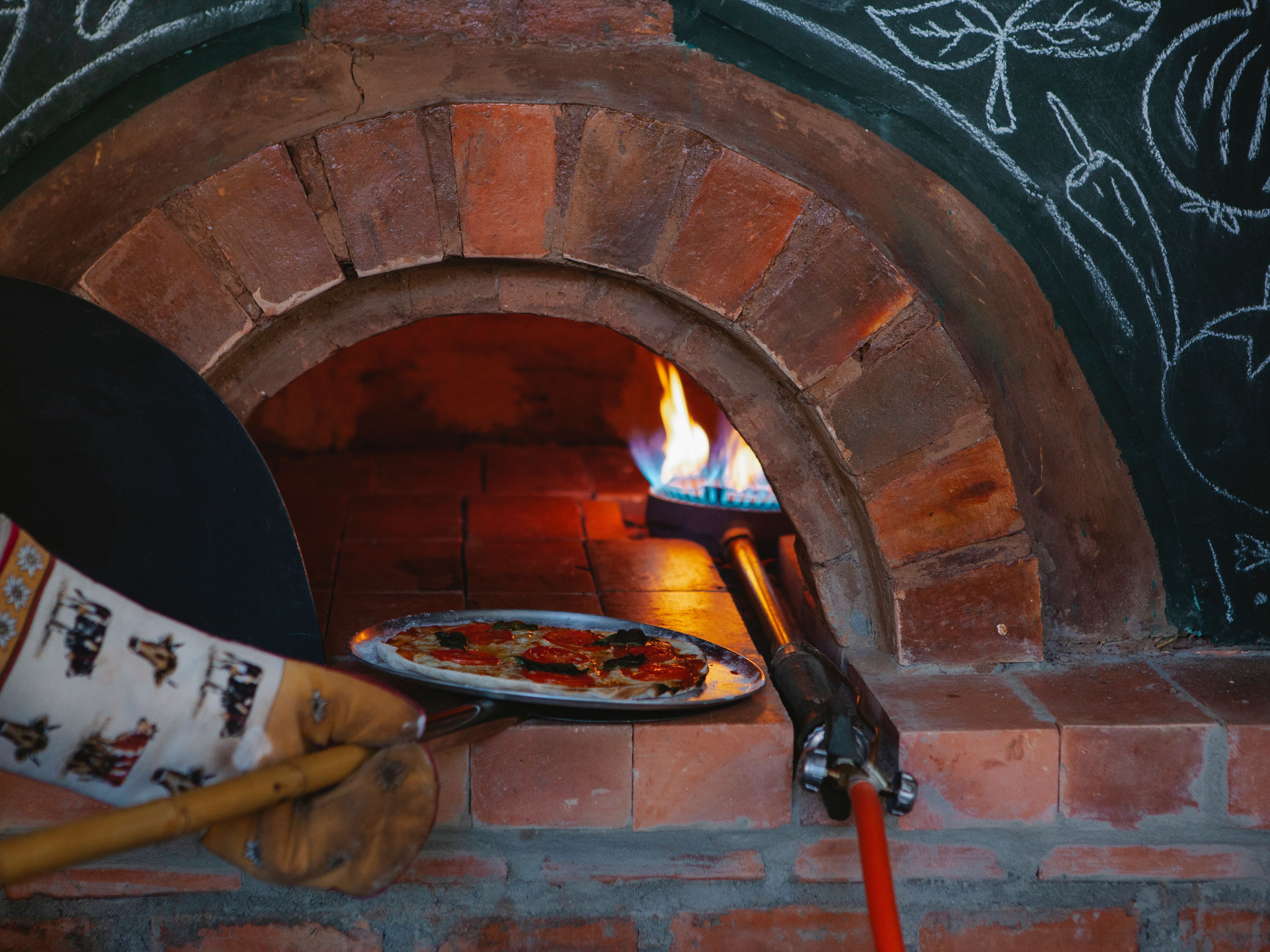 A pizza baking in the mouth of a wood-fired oven