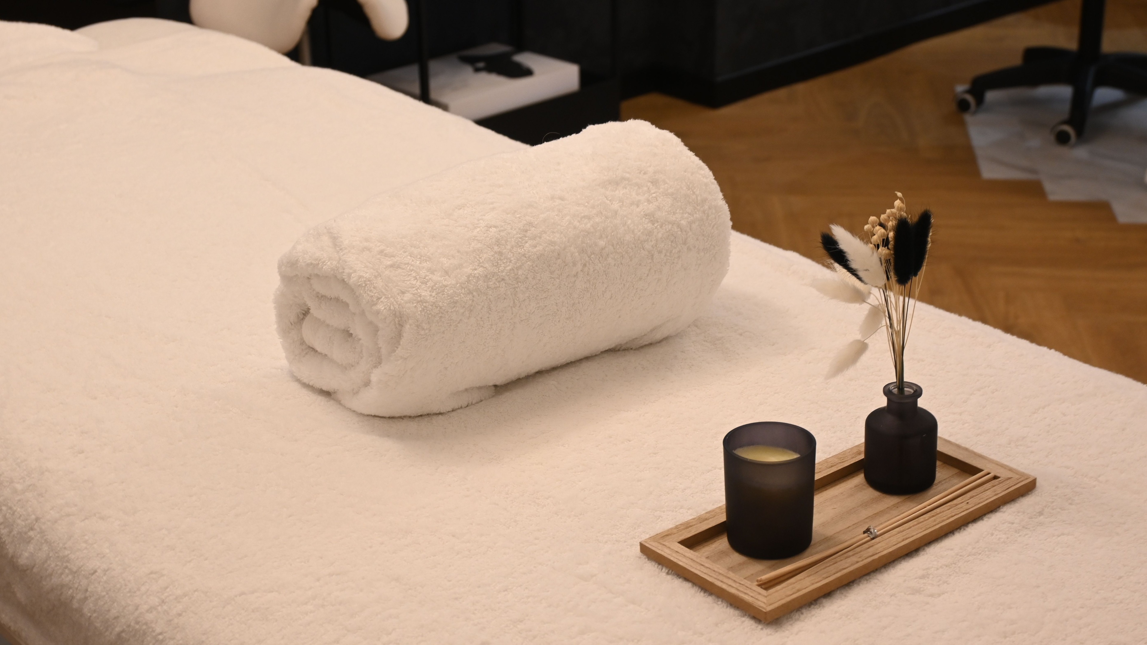 A treatment room with one bed, folded towels and a small ceramic vessel, no person present