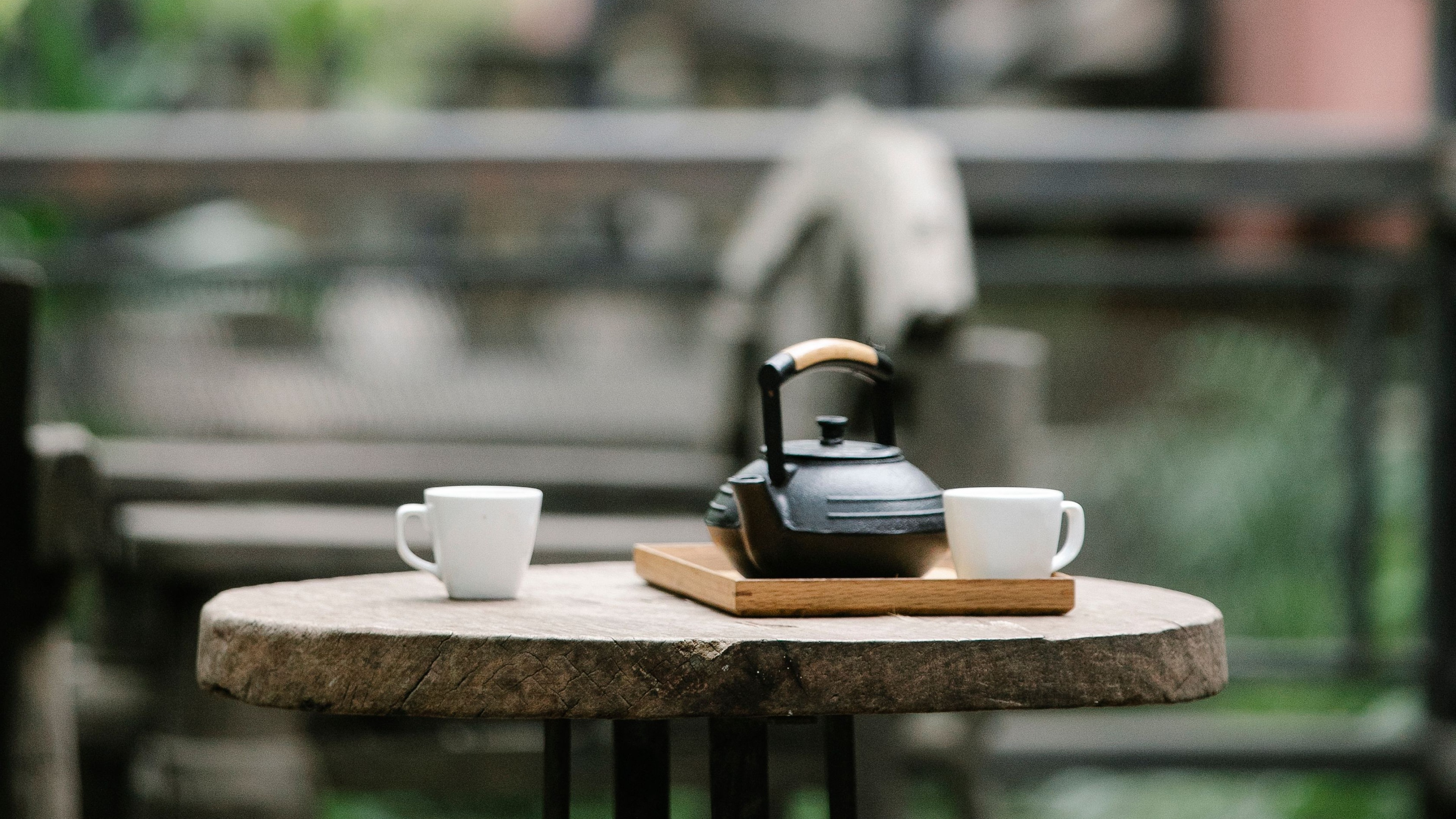 A ceramic teapot and cup on a low table, steam rising, an out-of-focus garden behind