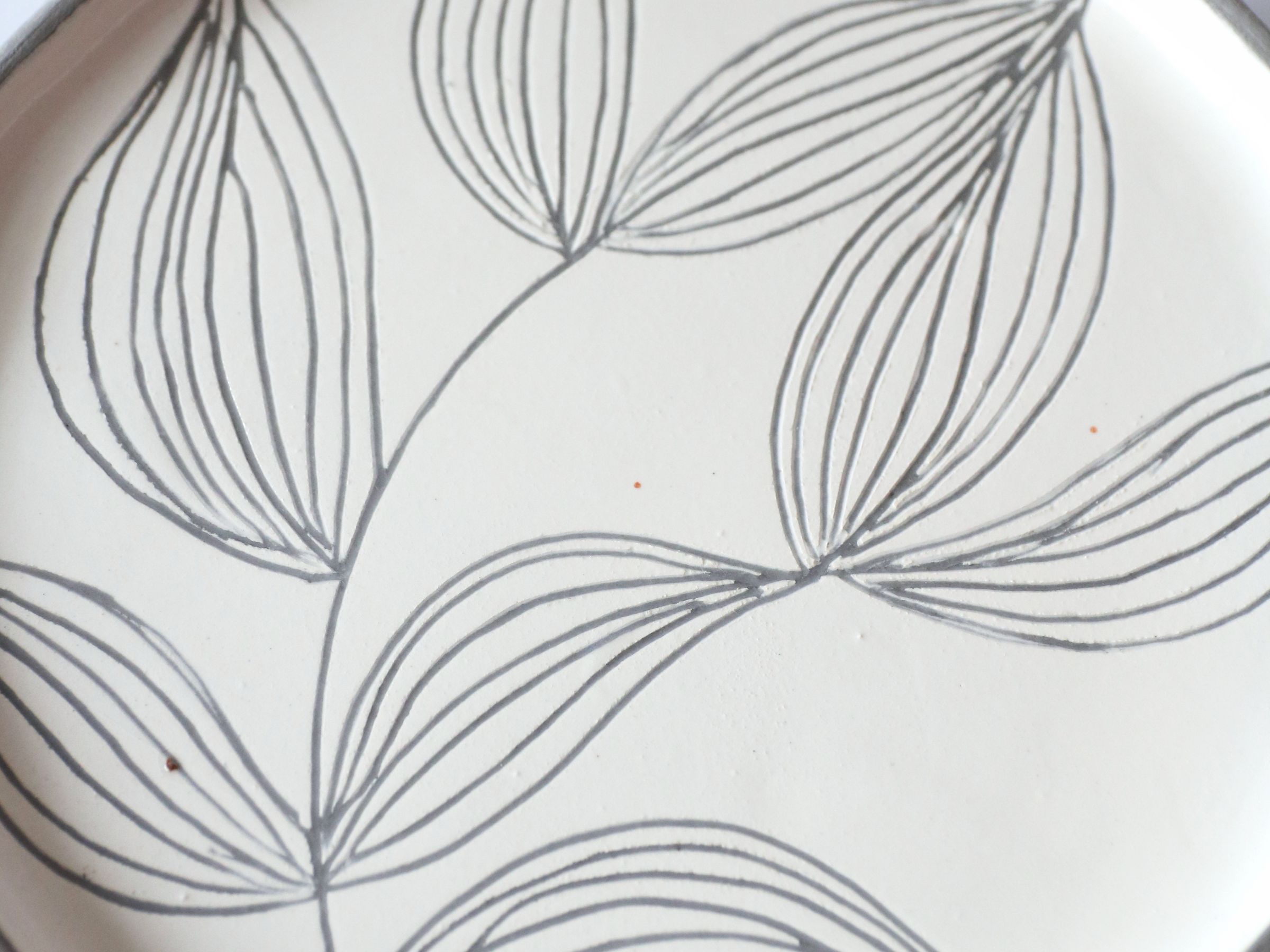 A single ceramic plate with a pressed leaf design, seen close up