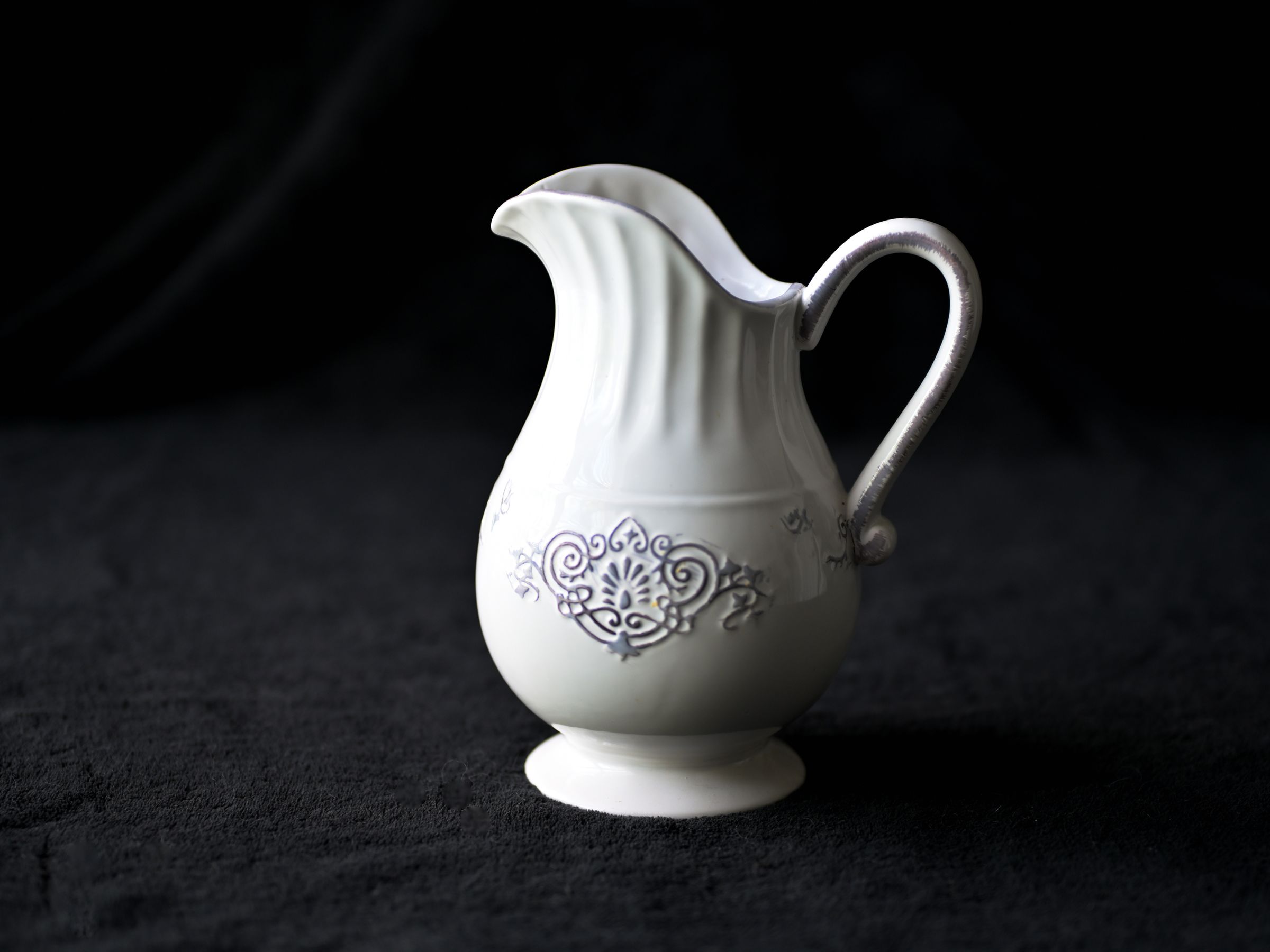 A white ceramic pitcher with moulded detailing against a dark backdrop