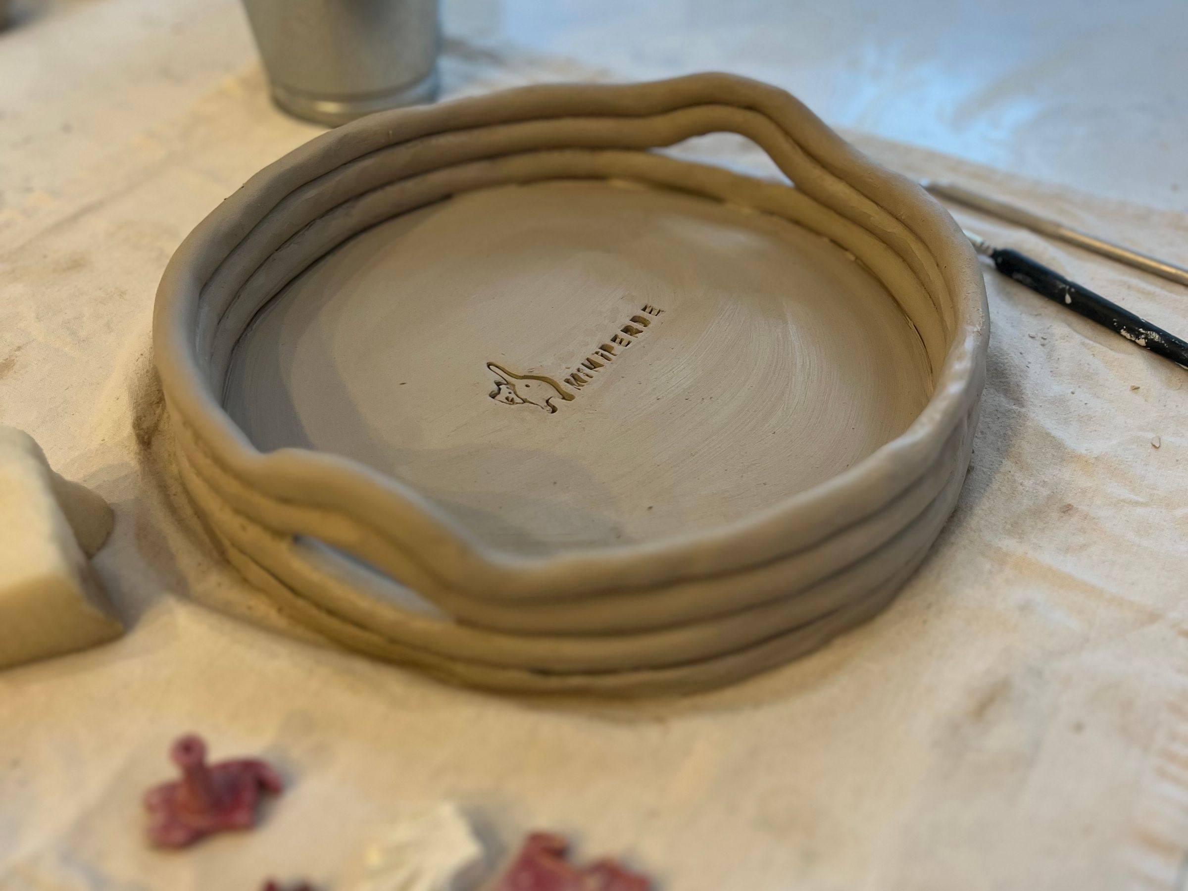 A handmade pottery platter on a workshop table beside its tools