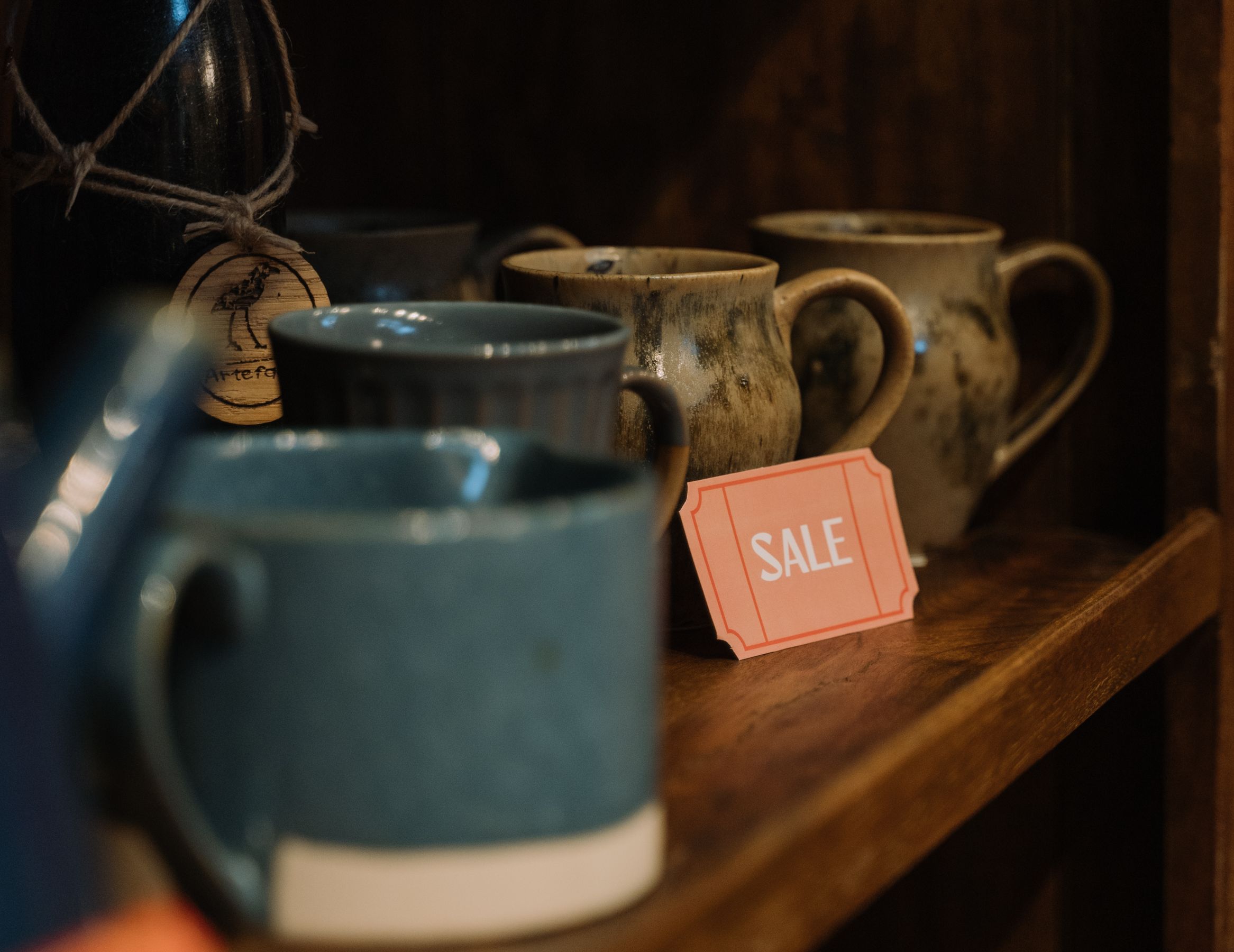 Ceramic cups lined up on a wooden shelf with handwritten sale signs