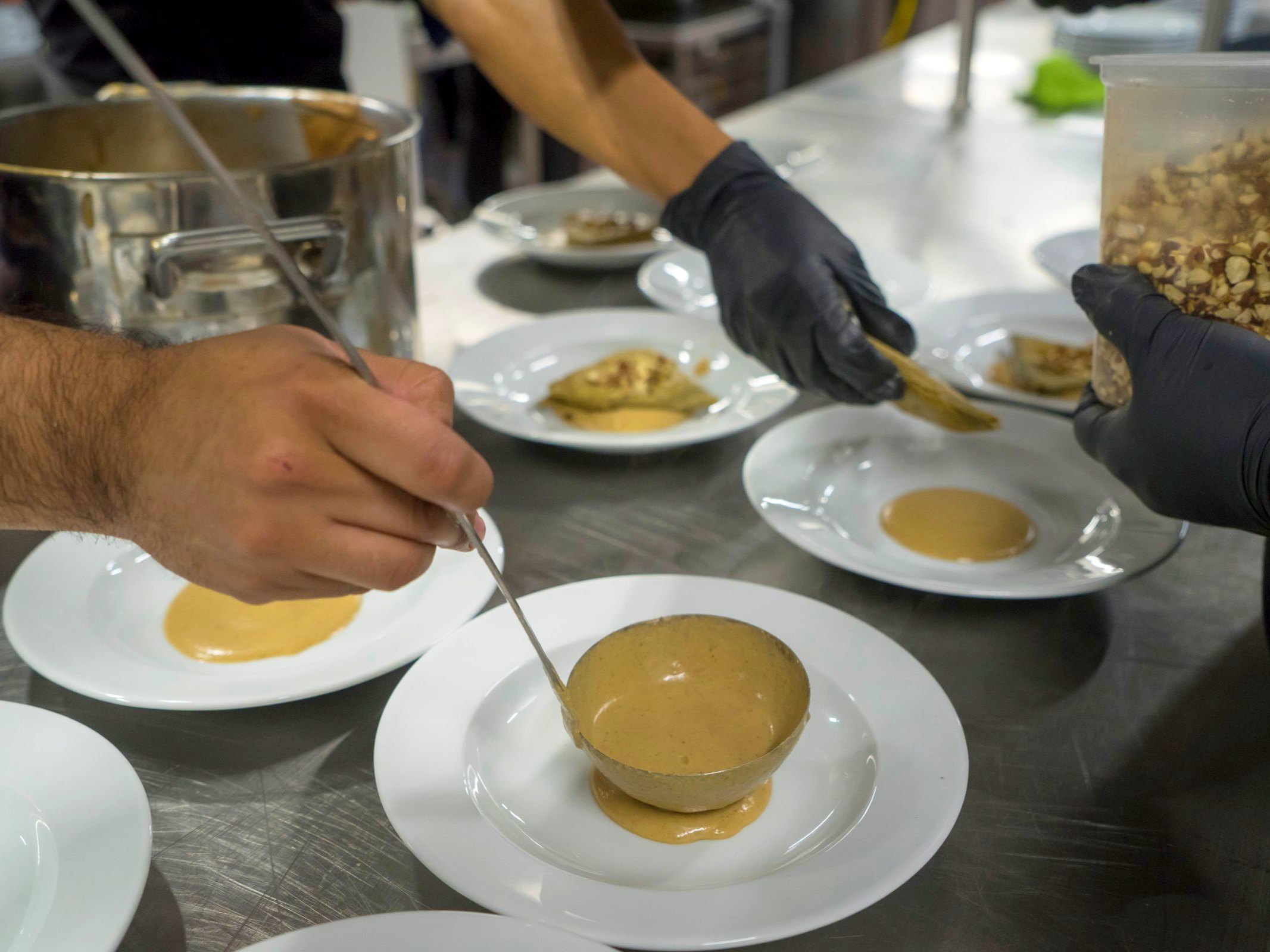 The pass at service, a chef plating under a heat lamp, steam, hands only